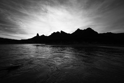 Black-and-white view of a silhouetted canyon skyline above rippled river water, an oar blade at the edge.
