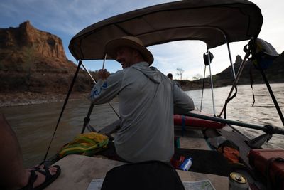 Oarsman in a straw hat and sun hoodie rowing, a red sandstone tower rising behind.