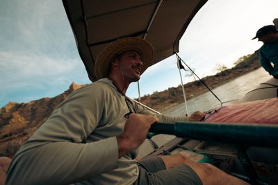 A rower works the oars under a shade canopy, warm evening light on the canyon wall behind.