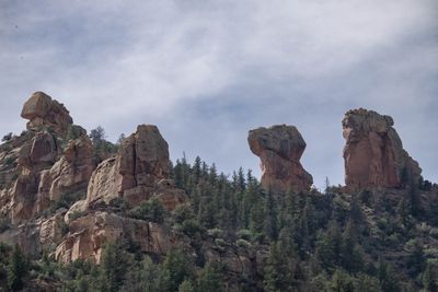 Balanced sandstone towers stand along a wooded ridge above dark conifers under an overcast sky.