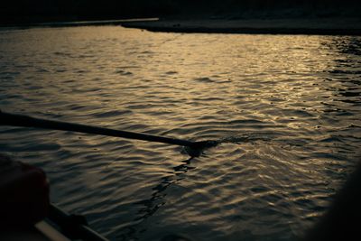 An oar blade slices into water lit gold by low sun, its wake curling behind.