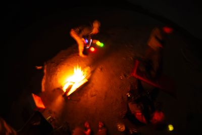 Crew gathered around a beach campfire at night seen from above, glow sticks scattered on the sand.