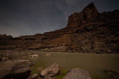 Stars above a moonlit sandstone butte, the river below still around boulders in the shallows.