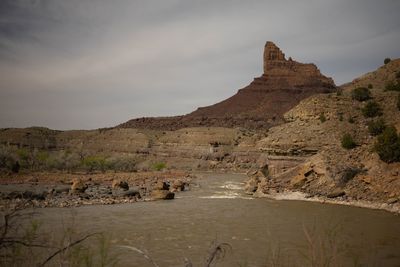 The river pushing through exposed boulders below a stepped sandstone tower at the approach to Three Fords Rapid.