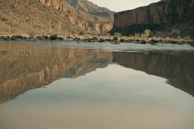 Canyon walls and a boulder bar doubled in a perfect mirror reflection on still water.