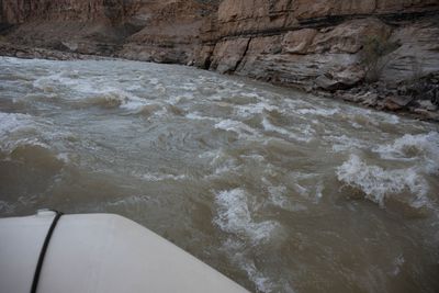 View from the bow of a raft running a rapid, whitewater churning below layered canyon walls.
