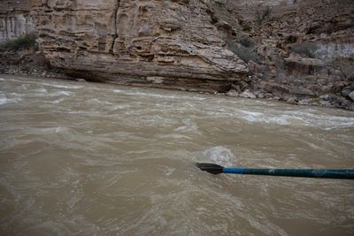 An oar blade digs into whitewater mid-rapid, an eroded sandstone wall behind.
