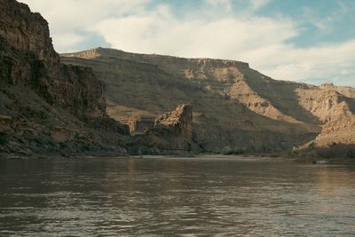 An isolated sandstone pillar stands mid-canyon where the river widens, a layered mesa behind it.