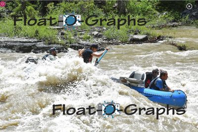 In a churning Snake River rapid a crew member stands waist-deep in the whitewater hauling on a blue oar while another person is in the water to the left, and the blue raft floats off to the right with two crew aboard, a bedrock shelf and green brush along the bank.