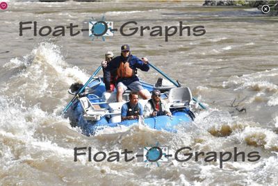 Near-duplicate head-on frame of the blue oar raft in a wide silty Snake River rapid, the rower on both oars in an orange PFD with a crew member behind him and two riding the bow tube, brown boils and whitewater on all sides.
