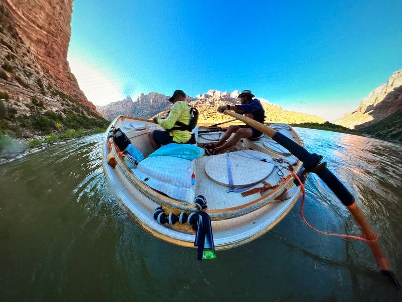Two men ride a wooden dory down a calm stretch of the Green River through Split Mountain